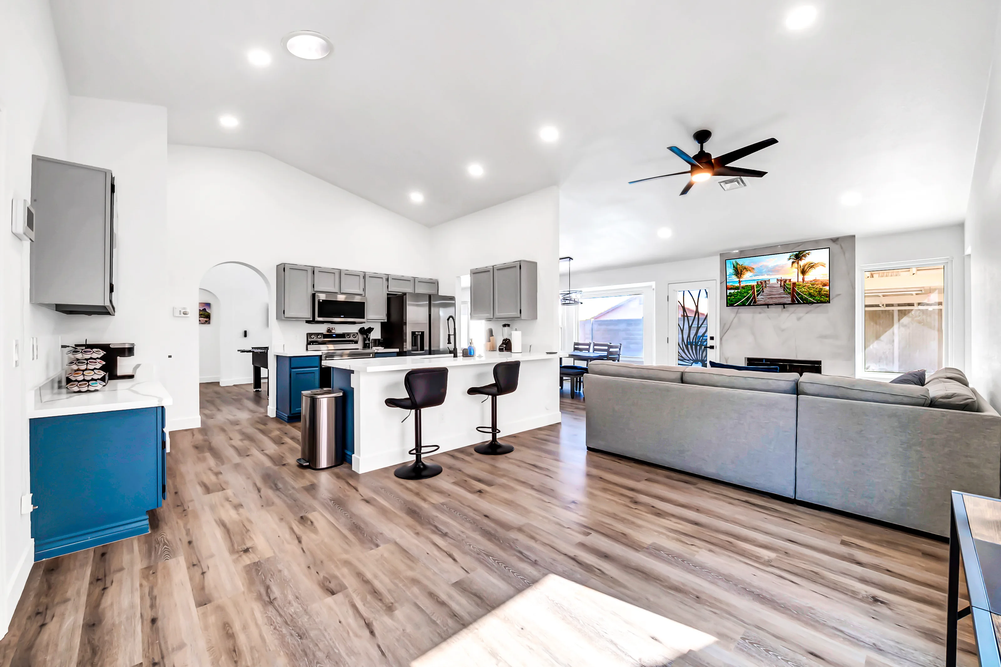 The home's bright open-concept shared space, with the kitchen island, breakfast bar seating, and living room sectional together under vaulted ceilings.