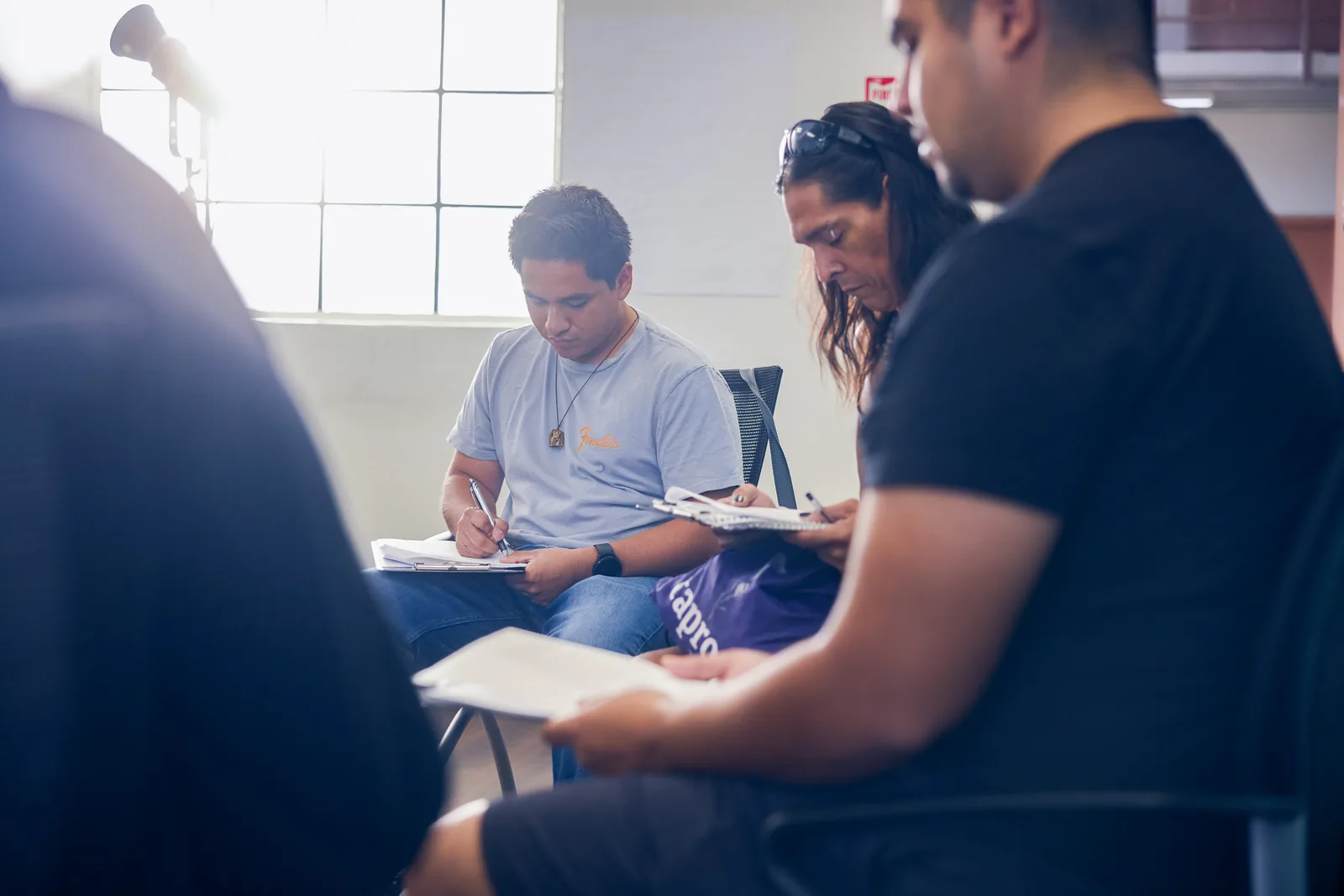 Participants take notes during a group session in a sunlit room.