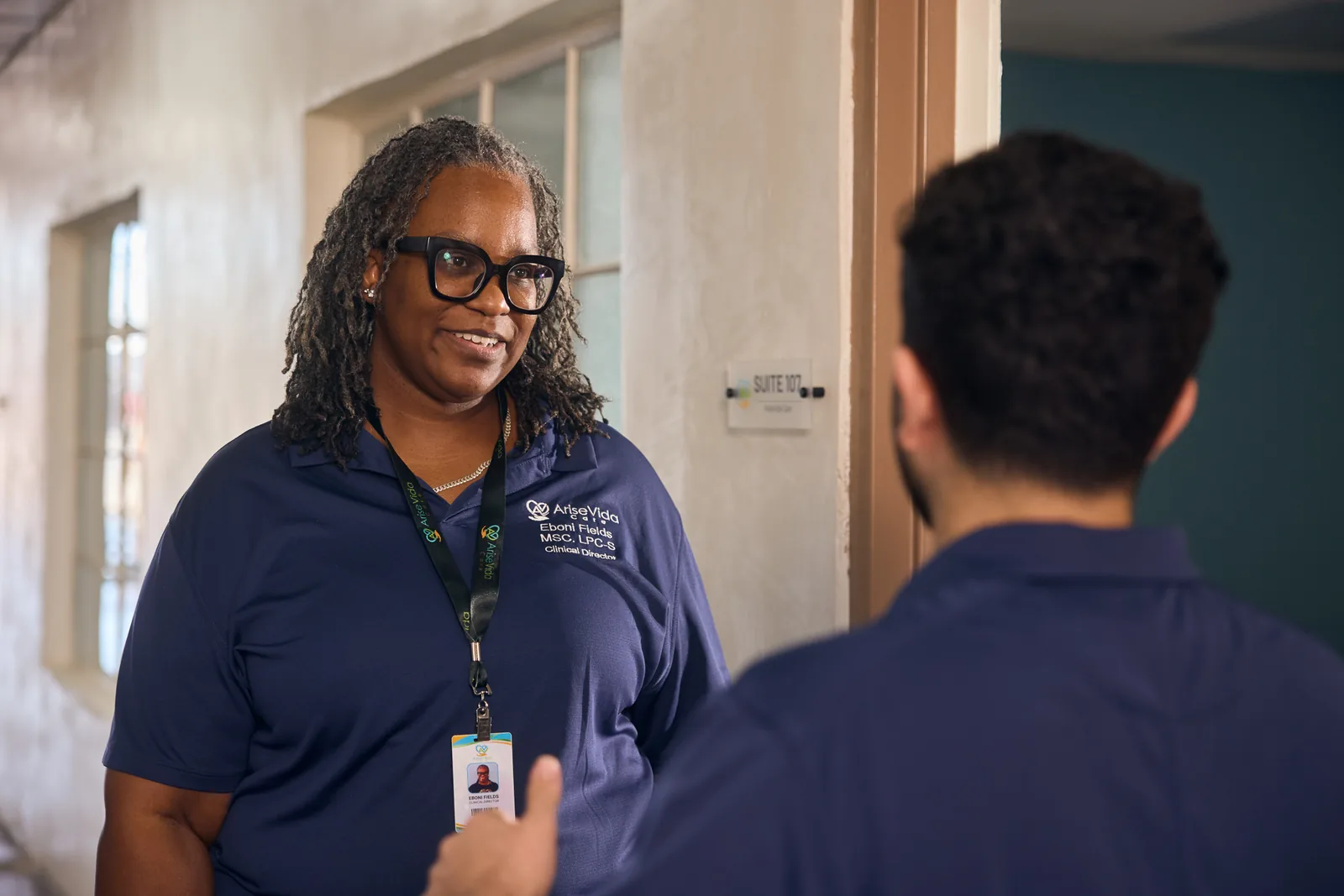 AriseVida Care team member smiling while speaking with a client in a clinic hallway.