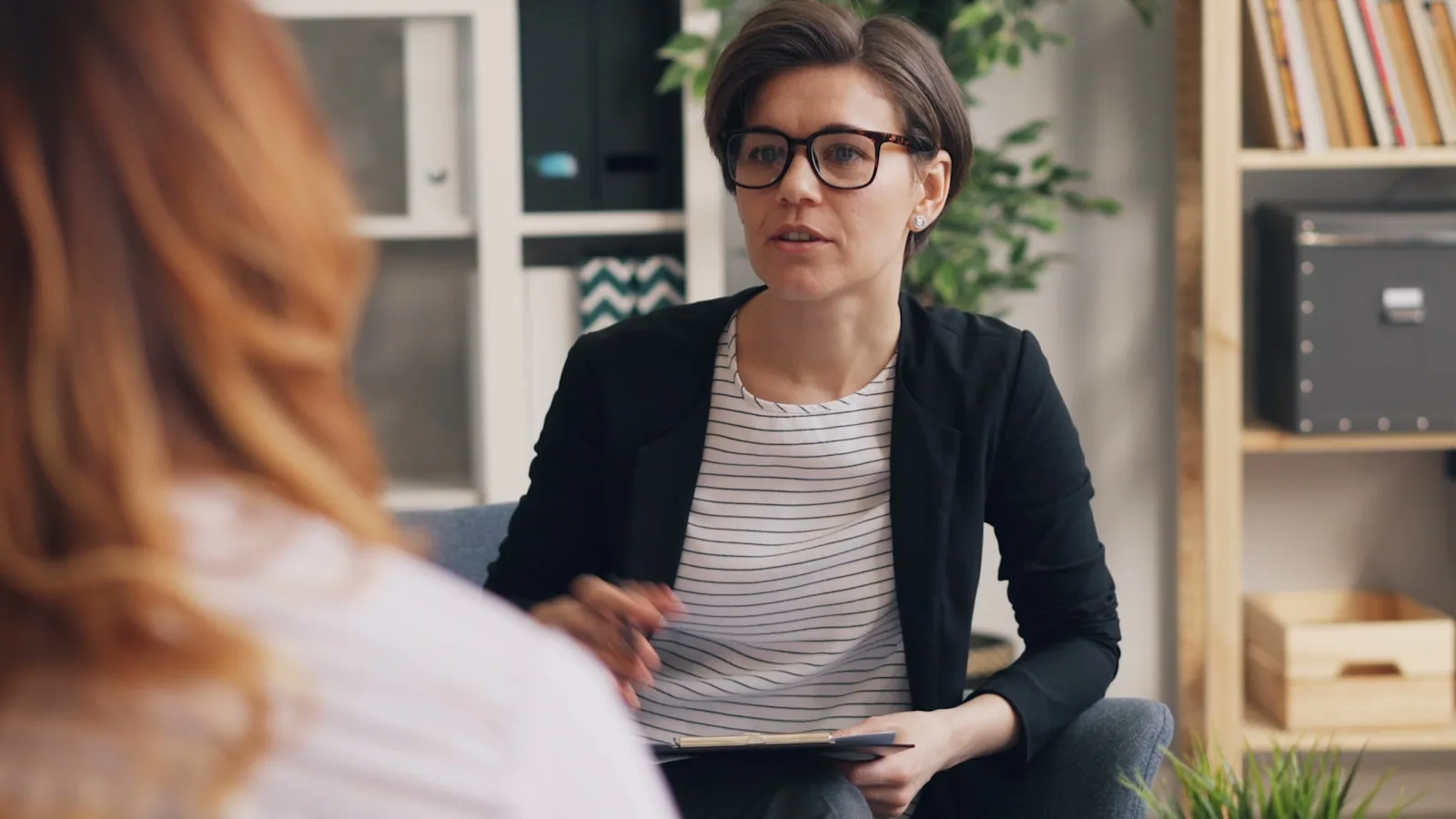 A woman sitting on a couch talking with another woman.