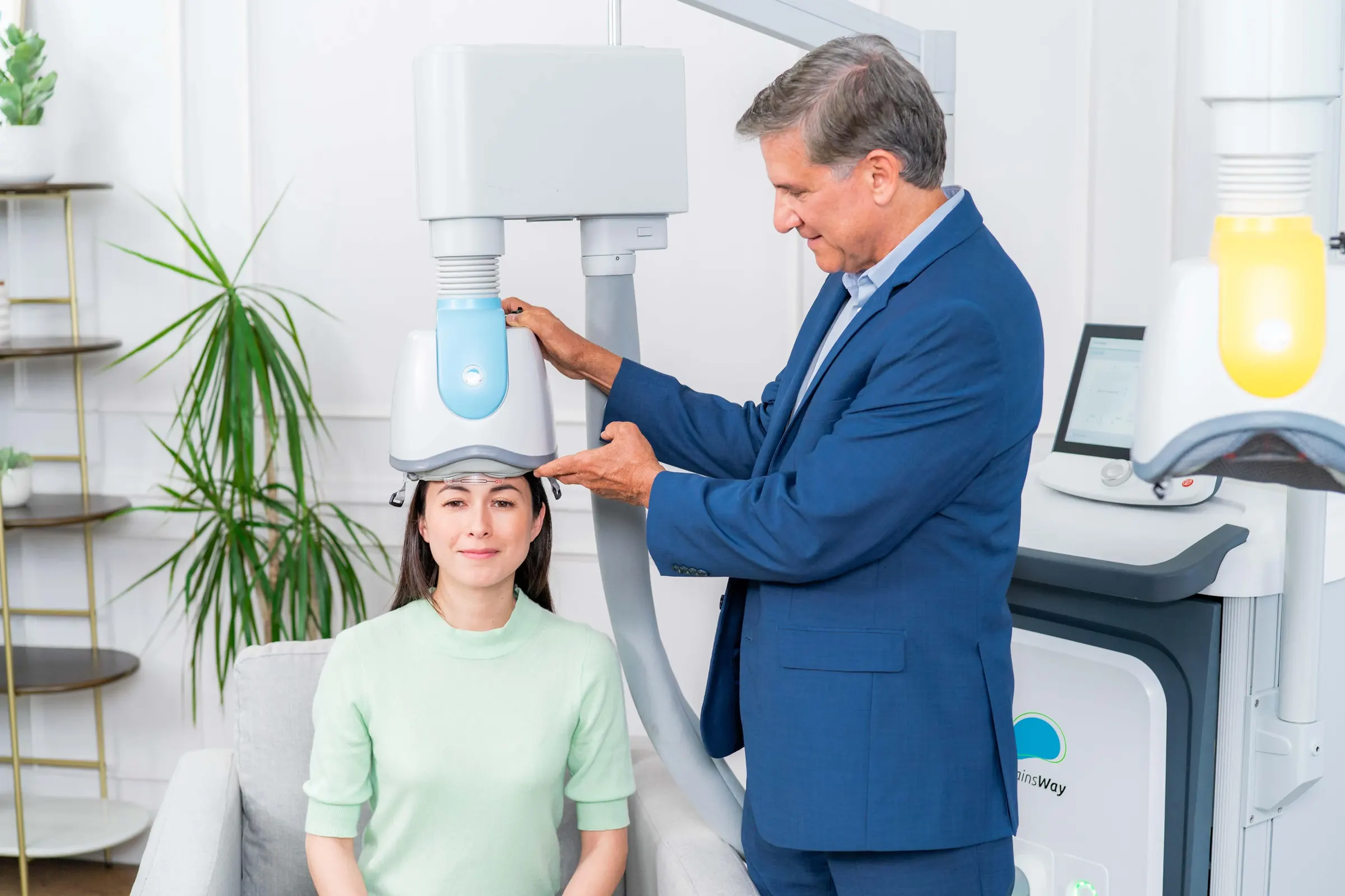 A seated patient wearing a BrainsWay Deep TMS helmet during a clinical session at AriseVida Care.