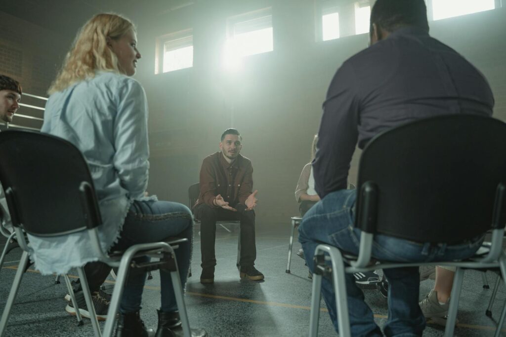 A diverse group of adults in a supportive discussion setting indoors with sunrays.